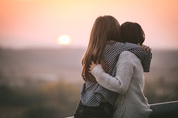Two women hug while looking at a sunset